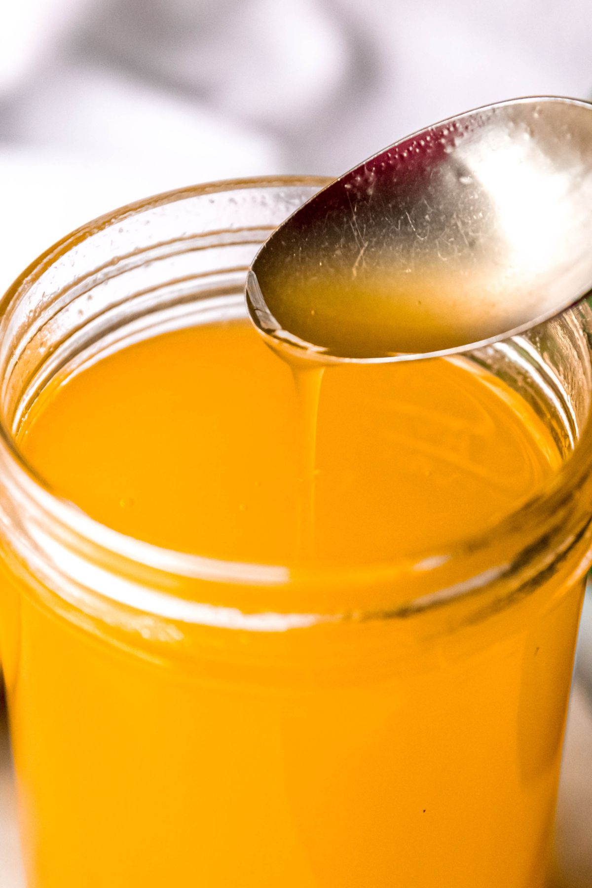 closeup shot of a silver spoon drizzling mango simple syrup into a mason jar showing how viscous it is. 