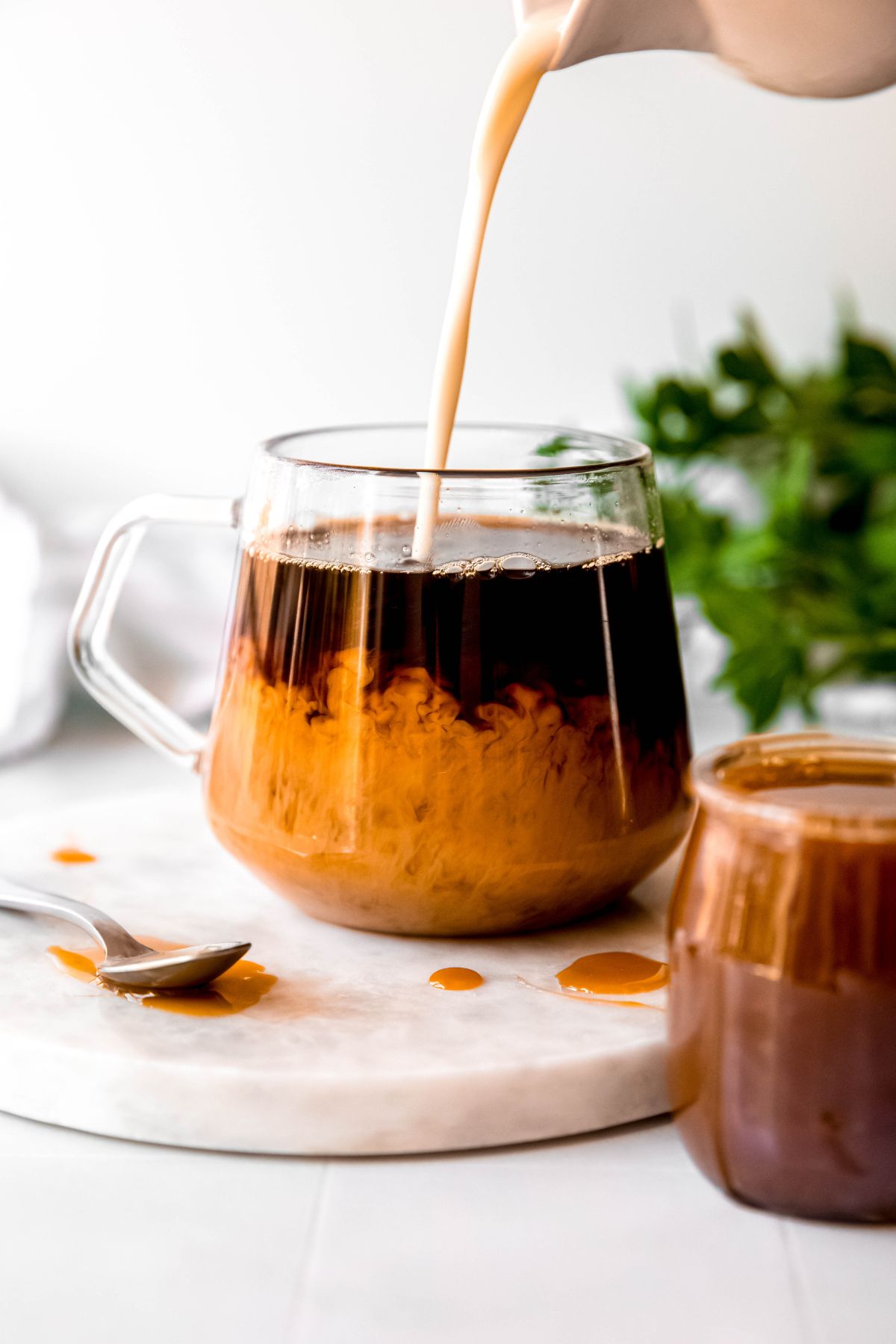 action shot of homemade caramel macchiato creamer being poured into a clear mug with freshly brewed black coffee; you can see the cream bubbling up from the bottom. 