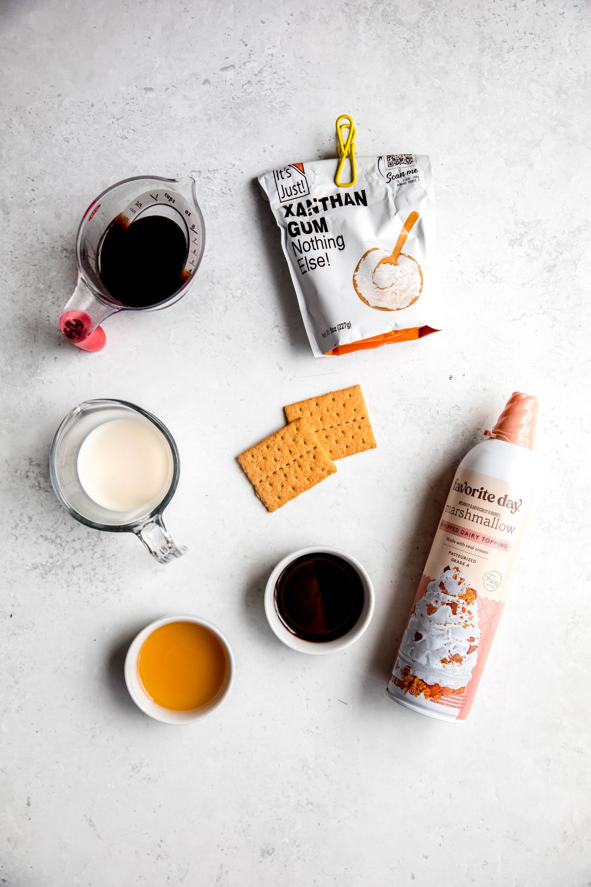 ingredients needed to make a homemade Starbucks s'mores frappuccino recipe measured out on a white table. 