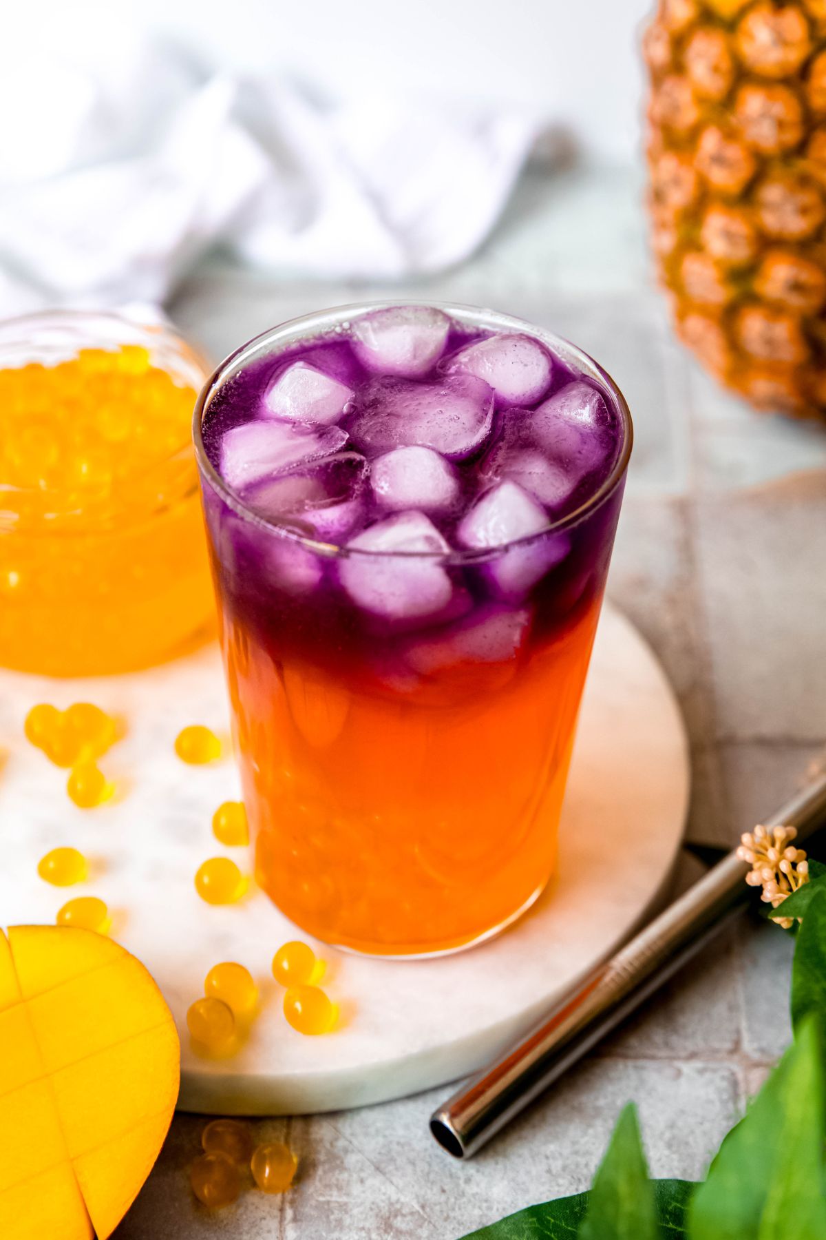 45 degree angle shot of a clear glass filled with a homemade starbucks tropical butterfly refresher showing the ombre hues going from magenta to orange to yellow popping boba.