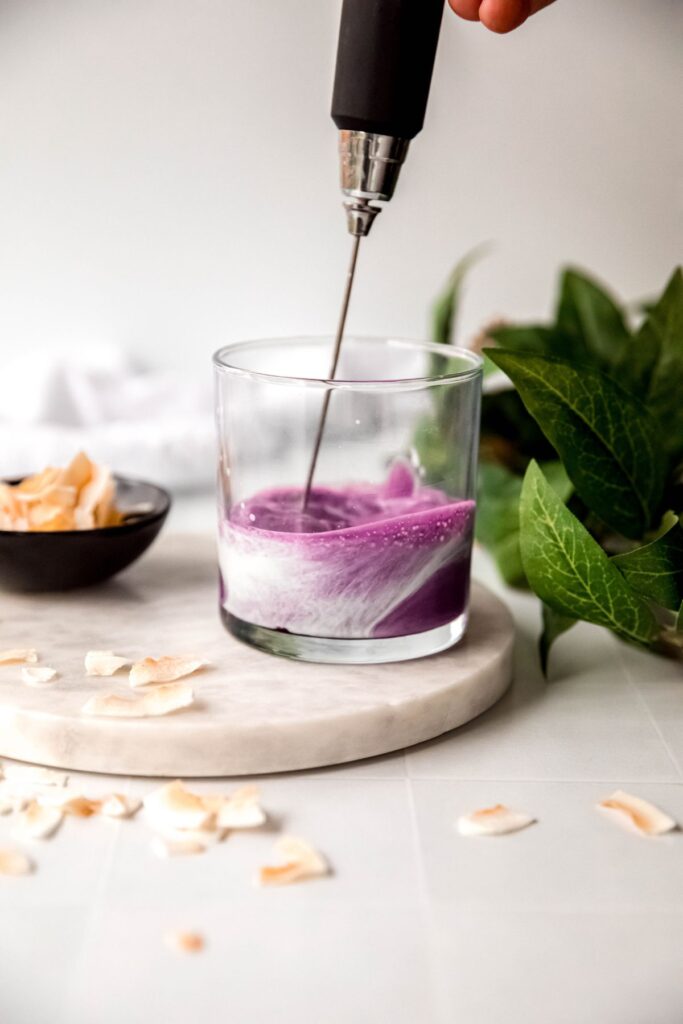 action shot of a milk frother whipping the ube coconut cold foam mixture in a small rocks glass. 