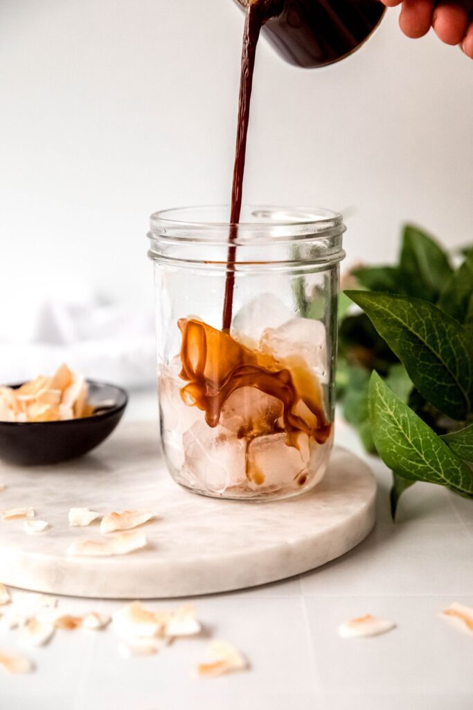 action shot of espresso being poured into a mason jar with ice.