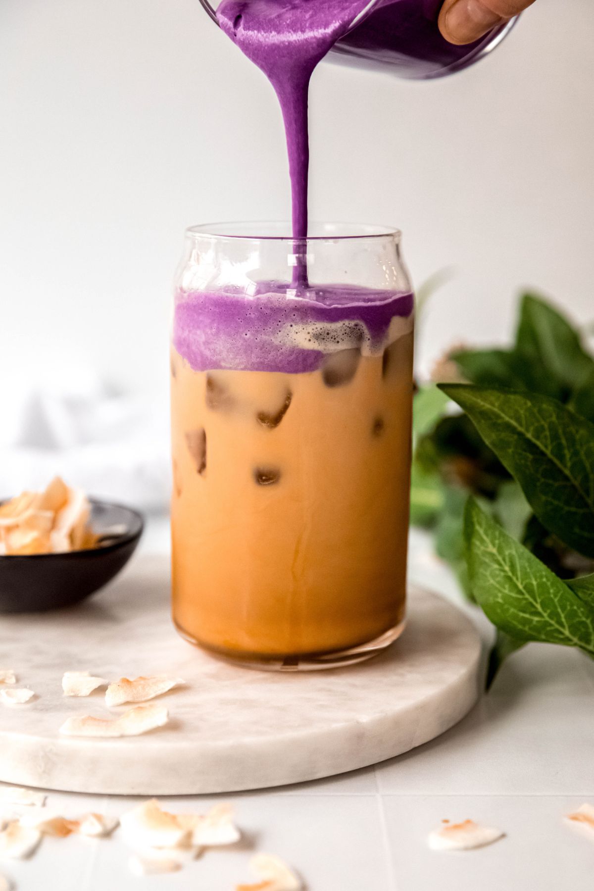 action shot of the ube coconut cream cold foam being poured on top of the iced coconut shaken espresso. 